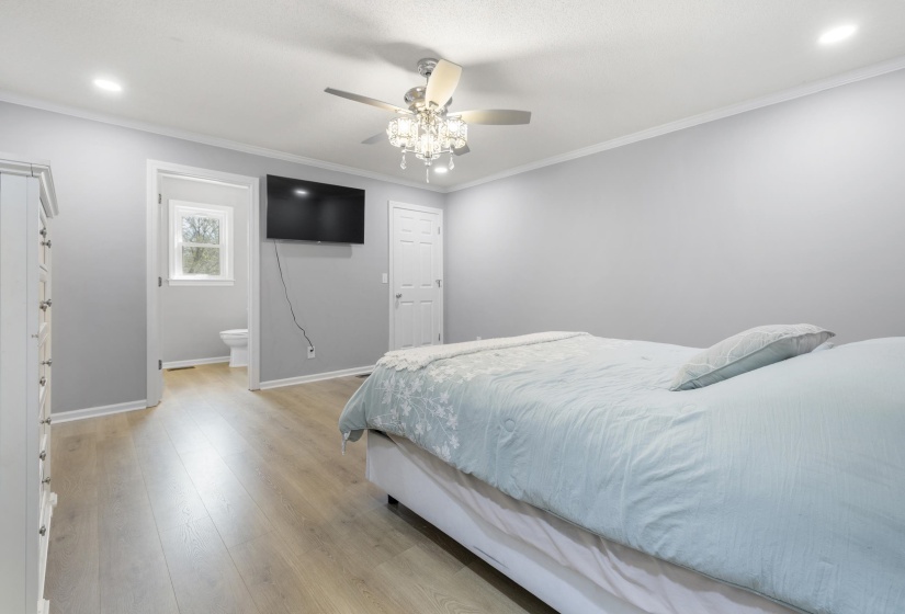 Bedroom featuring light wood-style floors, crown molding, a ceiling fan, ensuite bathroom, and recessed lighting
