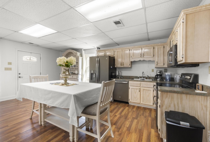 Kitchen with dark countertops, light wood finish cabinets, stainless steel appliances, a paneled ceiling, and dark wood finished floors