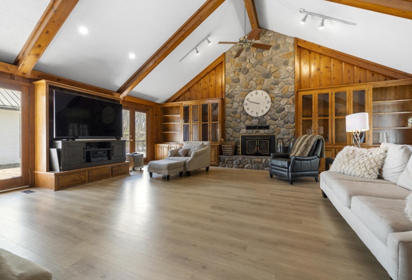 Family room featuring rail lighting, a stone fireplace, wood walls, wood finished floors, and ceiling fan