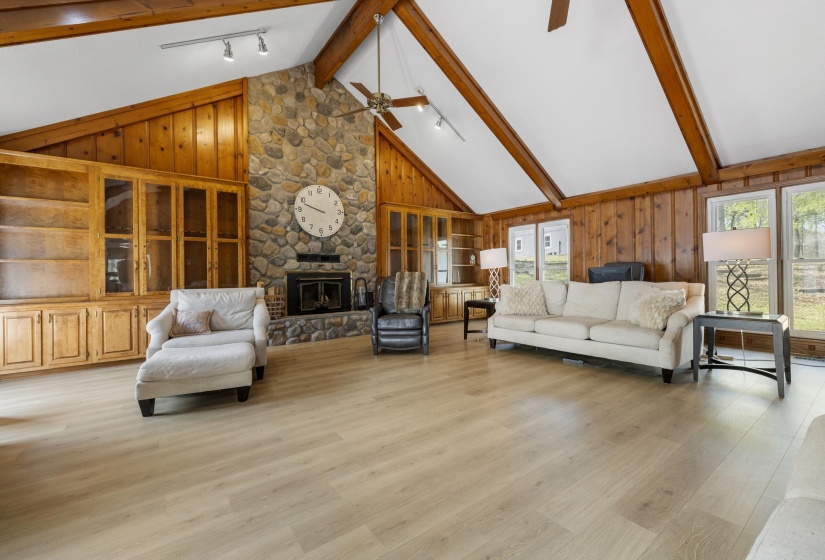 Family Room featuring wooden walls, rail lighting, a stone fireplace, light wood finished floors, and plenty of natural light