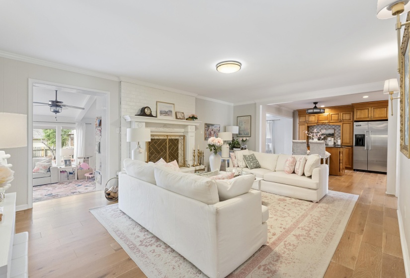Living room with a ceiling fan, light wood-type flooring, crown molding, and a fireplace with raised hearth