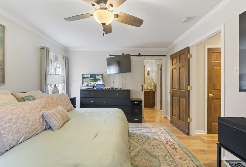 Bedroom with ensuite bathroom, light wood finished floors, ornamental molding, and a ceiling fan
