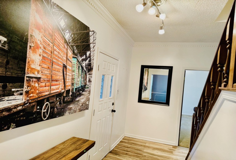 Foyer entrance featuring a textured ceiling, light wood-style flooring, and ornamental molding