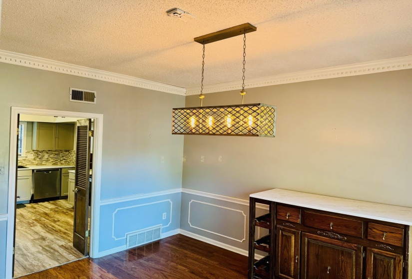 Unfurnished dining area featuring ornamental molding, dark wood-style floors, a textured ceiling, a decorative wall, and wainscoting