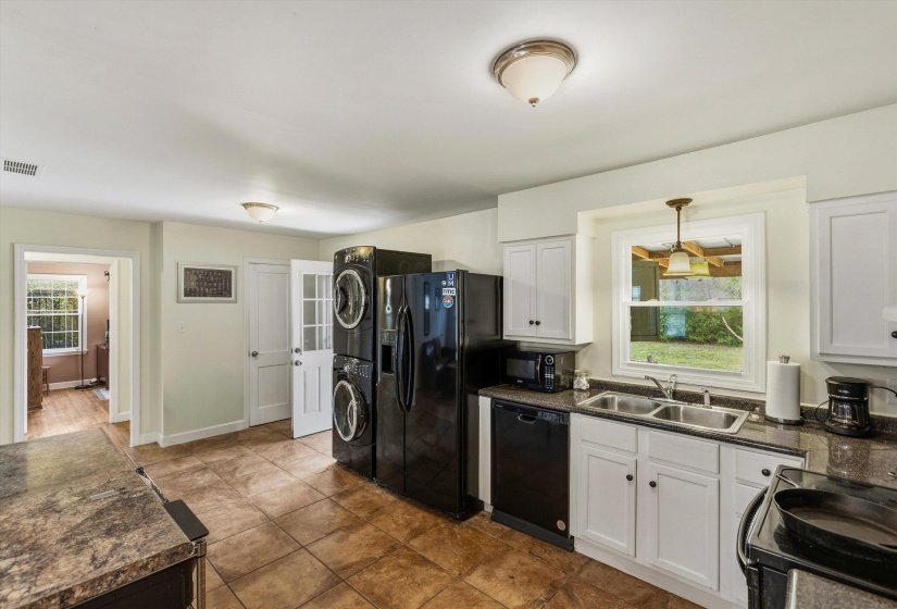 Kitchen with black appliances, white cabinets, decorative light fixtures, and dark counters