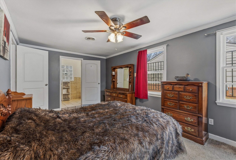 Bedroom with light colored carpet, crown molding, ceiling fan, and connected bathroom