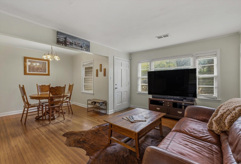 Living room with wood-type flooring, suspended lighting, and crown molding