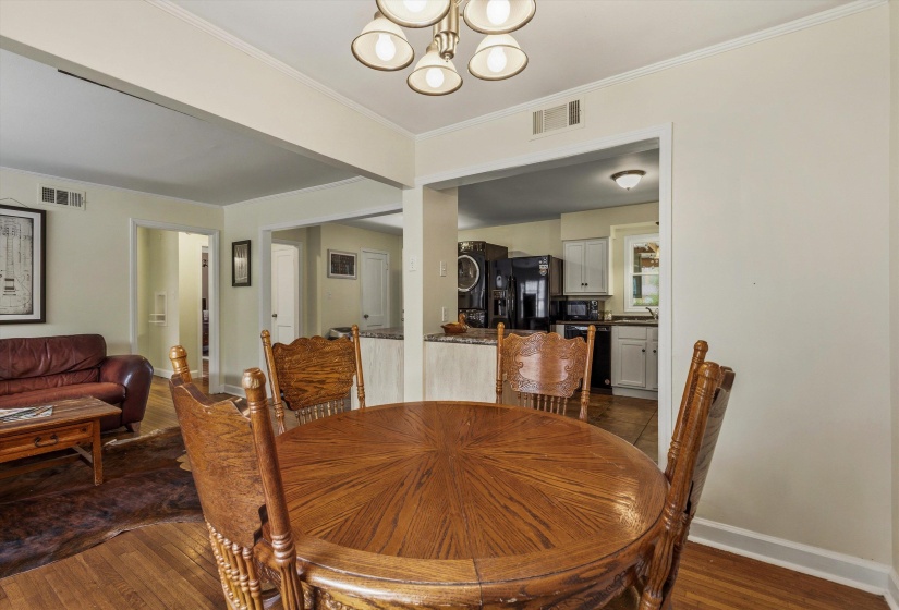 Dining room with hanging lights, dark wood-style floors, and ornamental molding