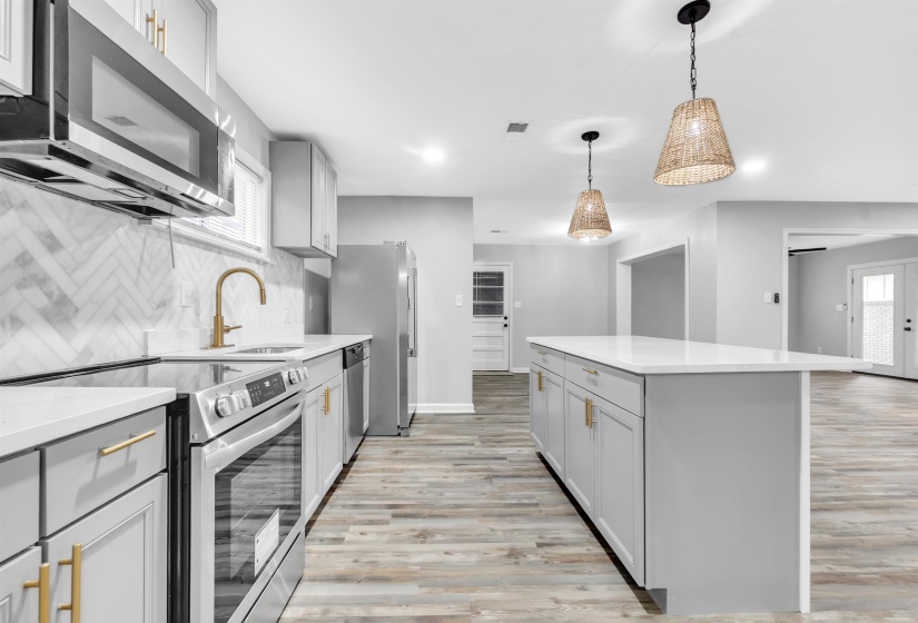Kitchen featuring appliances with stainless steel finishes, gray cabinetry, a sink, light wood-style floors, and a center island