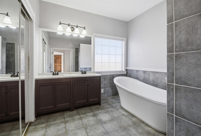 Full bath with double vanity, a freestanding bath, tile walls, and light tile patterned floors