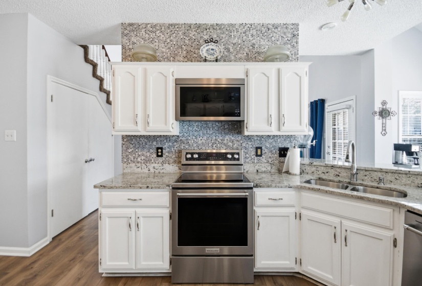 Kitchen featuring stainless steel appliances, light stone countertops, white cabinets, and a textured ceiling