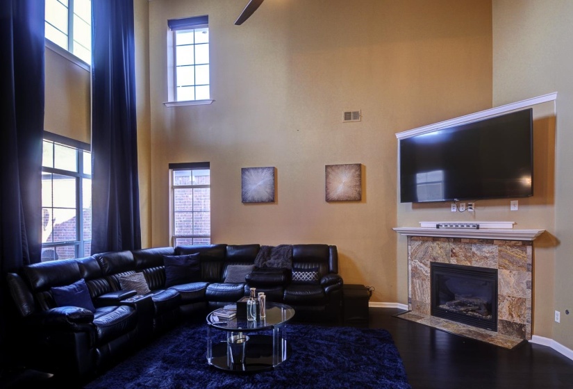 Living area with a tiled fireplace, a high ceiling, dark wood-type flooring, healthy amount of natural light, and a ceiling fan