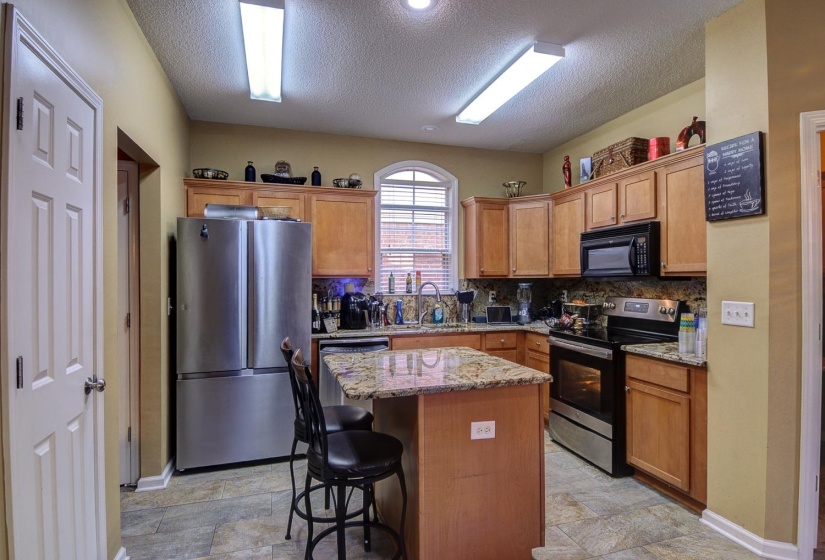 Kitchen featuring stainless steel appliances, light stone counters, a kitchen island, wood finish cabinetry, and a textured ceiling