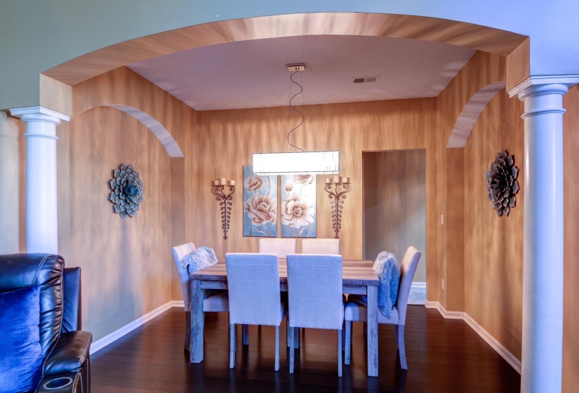 Dining space featuring decorative columns, arched walkways, and dark wood-type flooring