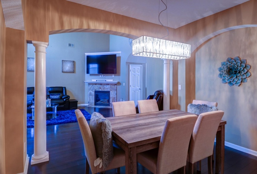 Dining space featuring decorative columns, dark wood-style flooring, arched walkways, and a tile fireplace