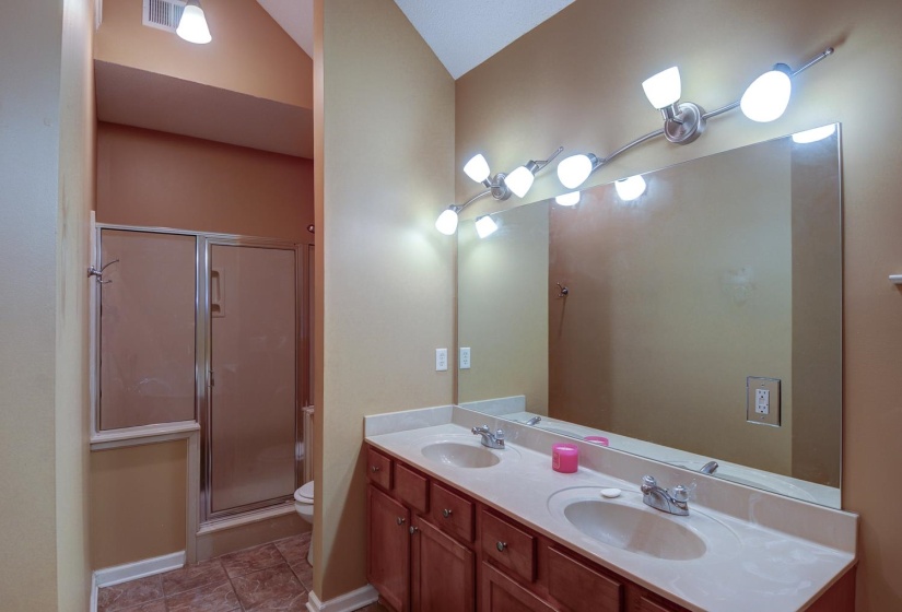 Full bathroom featuring double vanity, a shower stall, lofted ceiling, and tile patterned floors