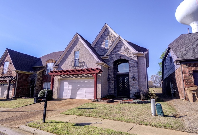 French country inspired facade with driveway, brick siding, a front yard, stone siding, and a garage