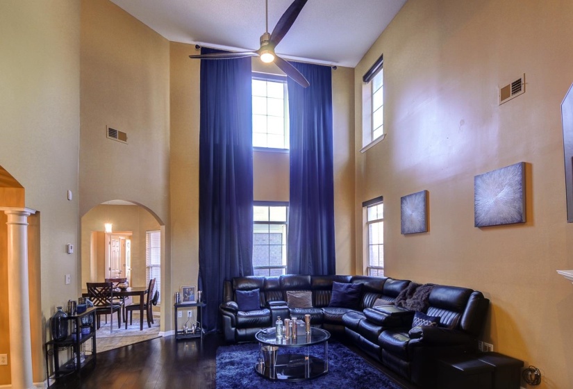 Living area with arched walkways, dark wood finished floors, ceiling fan, a high ceiling, and plenty of natural light
