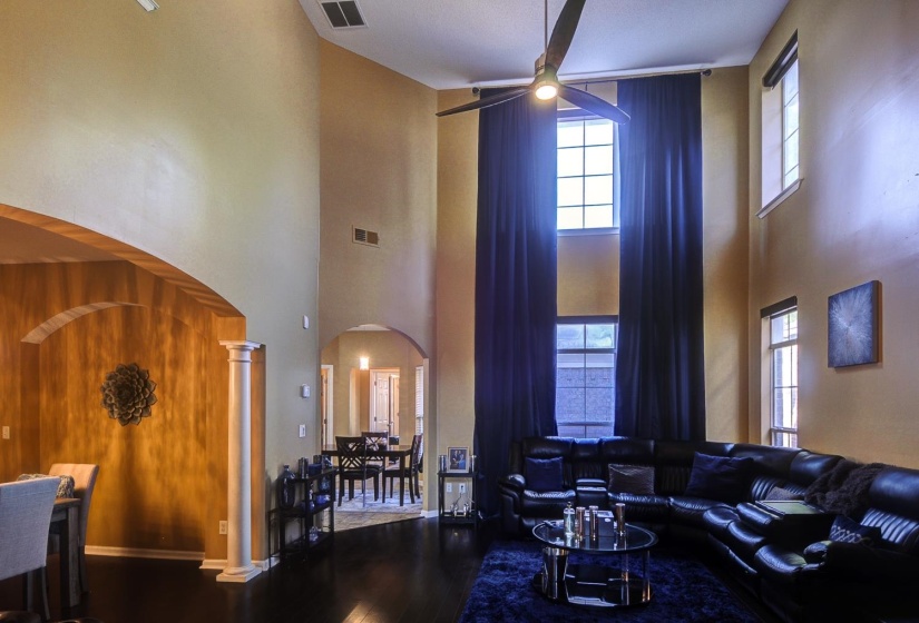 Living room with wood finished floors, a ceiling fan, a high ceiling, decorative columns, and arched walkways