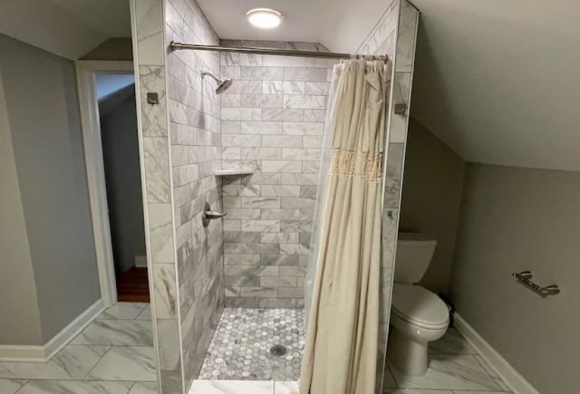 Bathroom featuring a shower with shower curtain, toilet, and lofted ceiling