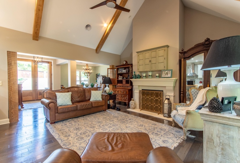 Living room with ceiling fan with notable chandelier, high vaulted ceiling, beam ceiling, french doors, and dark wood-type flooring