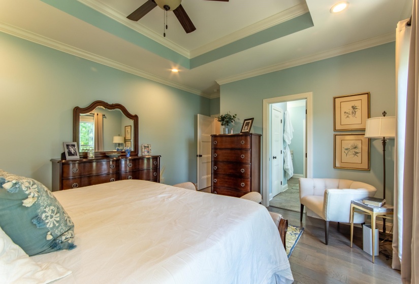 Bedroom featuring connected bathroom, hardwood / wood-style flooring, ceiling fan, ornamental molding, and a raised ceiling