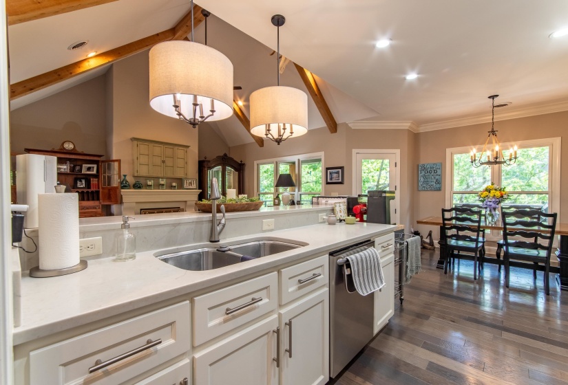 Kitchen with decorative light fixtures, stainless steel dishwasher, white cabinetry, vaulted ceiling with beams, and dark hardwood / wood-style floors