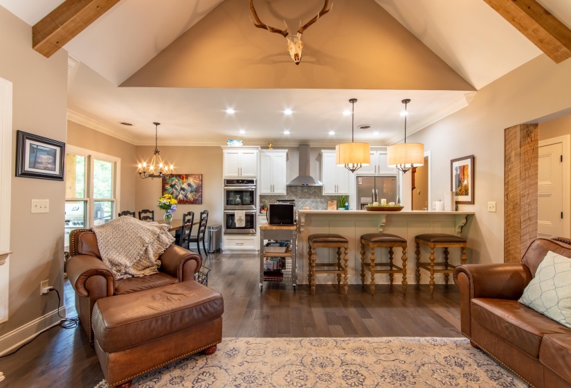 Living room featuring a notable chandelier, lofted ceiling with beams, crown molding, and dark wood-type flooring