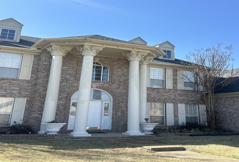 View of front facade featuring brick siding, a front lawn, a porch, and a shingled roof