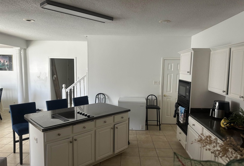 Kitchen with white cabinets, a kitchen bar, a textured ceiling, light tile patterned floors, and black appliances