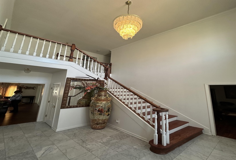 Stairs featuring suspended lighting, ornamental molding, marble look tiles, and a high ceiling