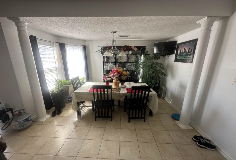 Dining space featuring decorative columns, a textured ceiling, and light tile patterned flooring
