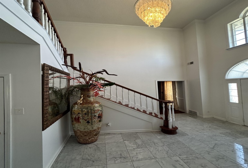 Entryway with a high ceiling, hanging lights, crown molding, and light marble finish flooring