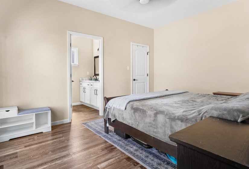 Bedroom with light wood-style floors, ensuite bath, and a ceiling fan