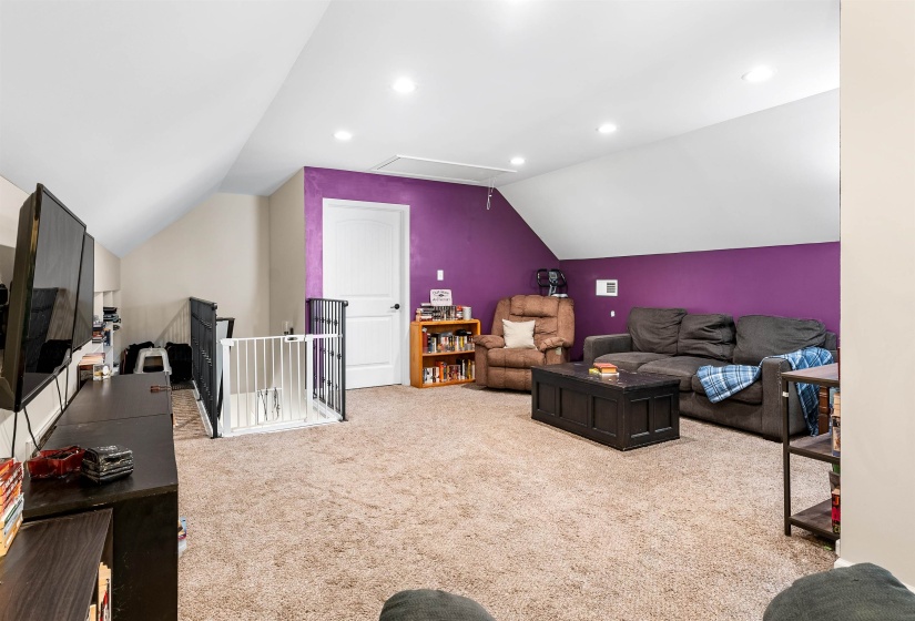 Living area with attic access, vaulted ceiling, light colored carpet, and recessed lighting