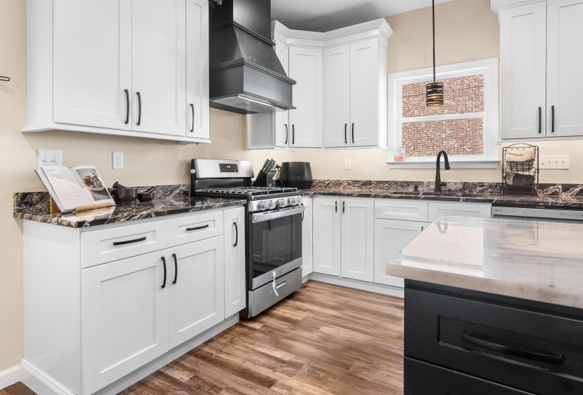 Kitchen featuring gas stove, dark stone counters, custom exhaust hood, white cabinets, and decorative light fixtures