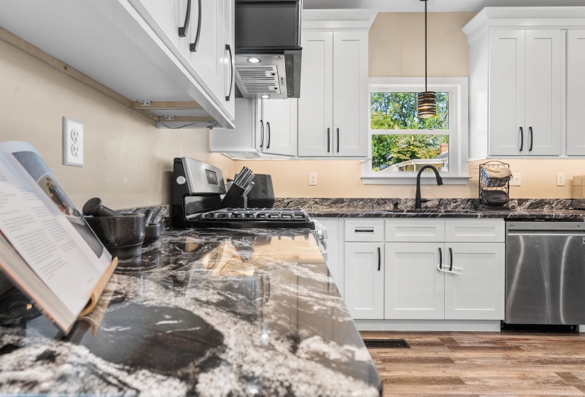 Kitchen with dark stone countertops, appliances with stainless steel finishes, white cabinetry, and extractor fan