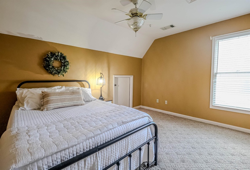 Carpeted bedroom featuring baseboards, visible vents, vaulted ceiling, and a ceiling fan