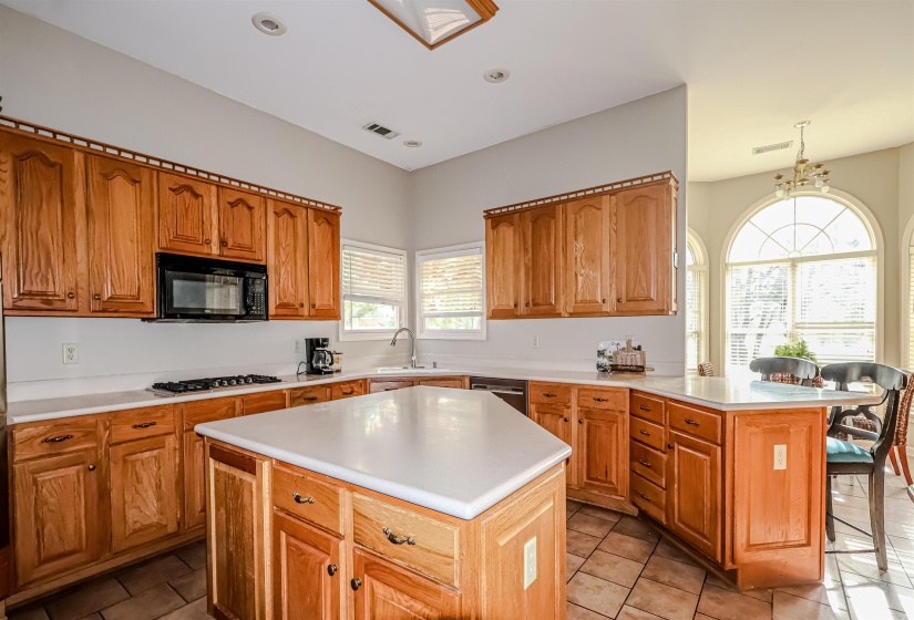 Kitchen featuring light countertops, a sink, black microwave, a peninsula, and gas stovetop