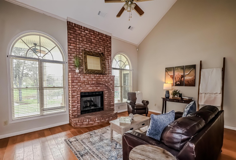 Living area featuring wood-type flooring, high vaulted ceiling, visible vents, a ceiling fan, and a fireplace