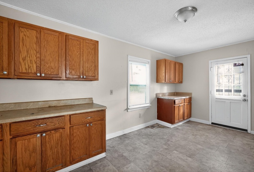 Kitchen featuring brown cabinets, light countertops, ornamental molding, and a textured ceiling