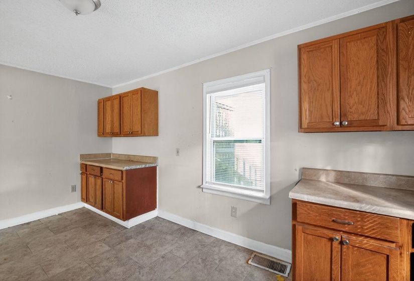 Kitchen featuring brown cabinets, crown molding, light countertops, and a textured ceiling