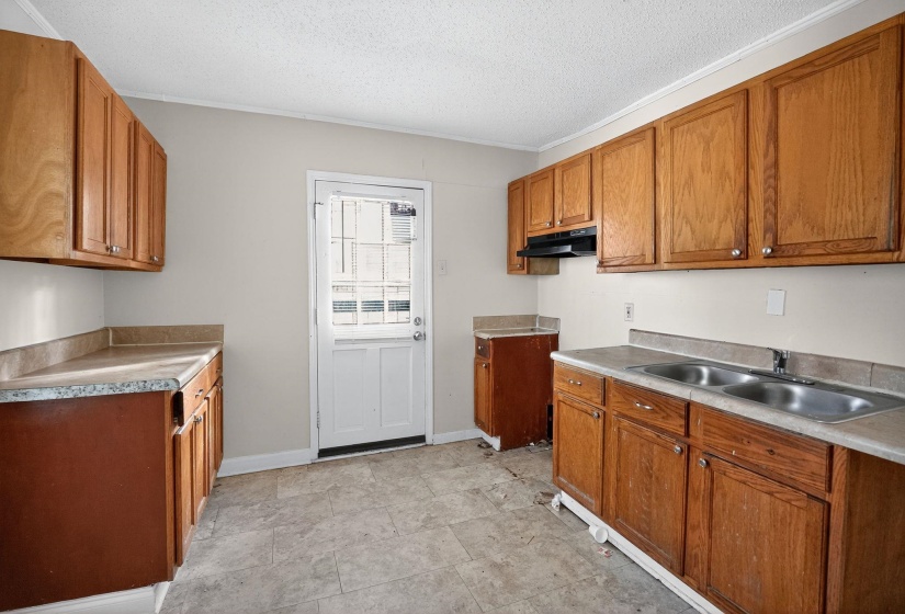 Kitchen with brown cabinets, a textured ceiling, light countertops, crown molding, and under cabinet range hood