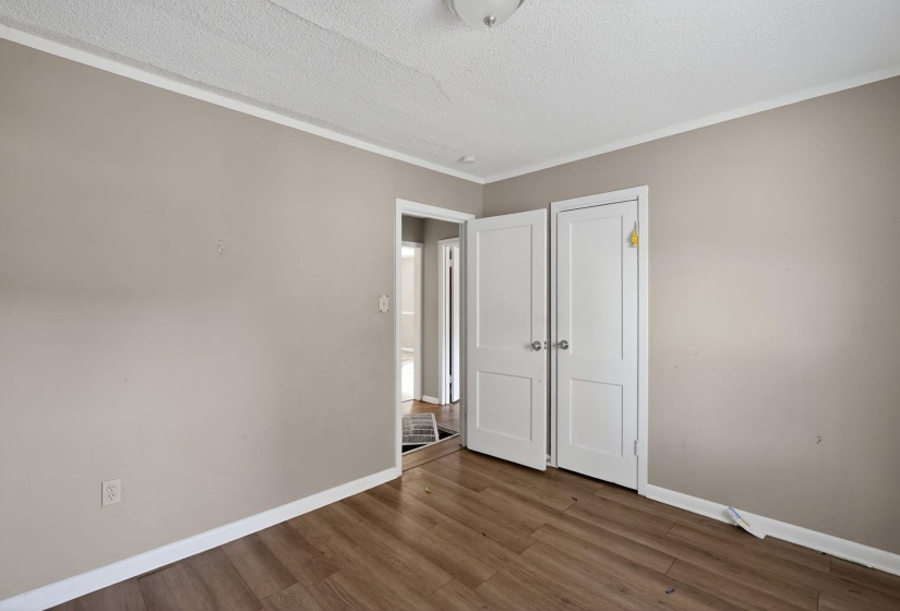 Unfurnished bedroom with a textured ceiling, wood finished floors, crown molding, and a closet