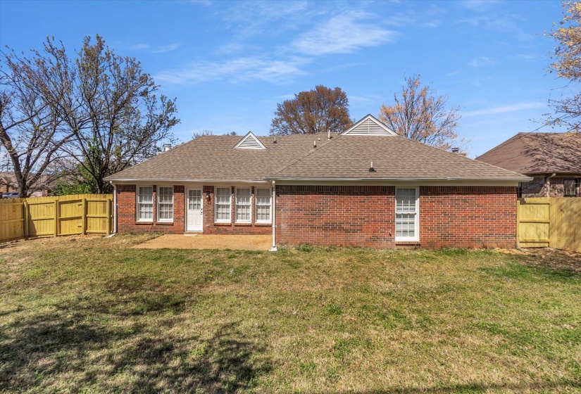 Rear view of house featuring a fenced backyard, brick siding, and a shingled roof