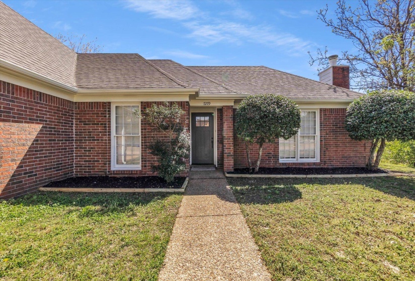 View of exterior entry with a chimney, a yard, brick siding, and roof with shingles
