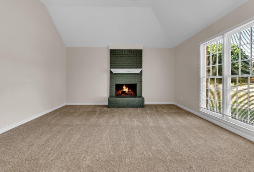 Unfurnished living room featuring a brick fireplace, vaulted ceiling, and light colored carpet