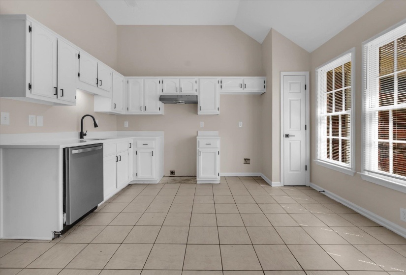 Kitchen featuring white cabinetry, dishwasher, light tile patterned floors, and lofted ceiling