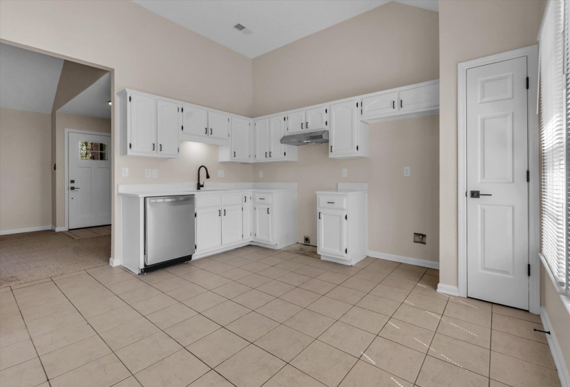Kitchen featuring stainless steel dishwasher, white cabinets, light countertops, light tile patterned flooring, and lofted ceiling