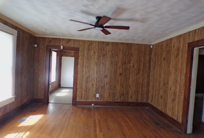 Empty room with dark wood-style floors, wooden walls, ceiling fan, and crown molding
